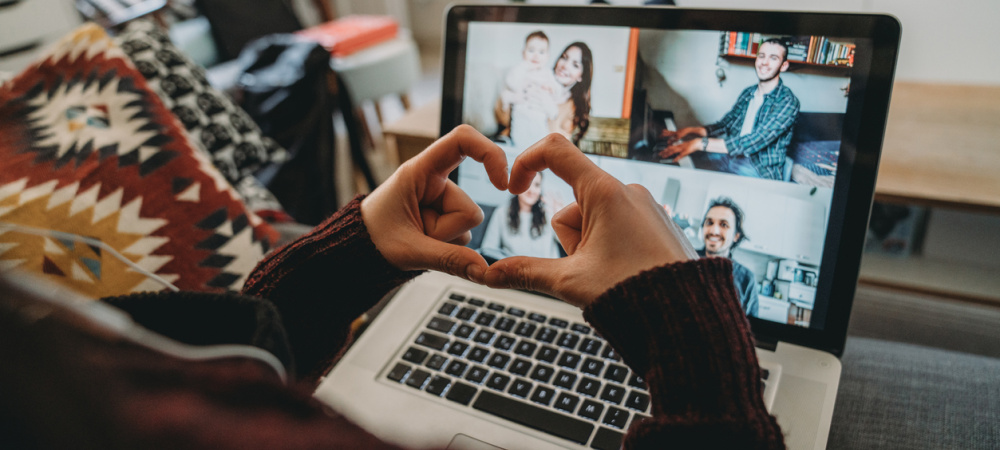 Frau zeigt ein Herz mit ihren Händen vor dem Laptop, Videotelefonat