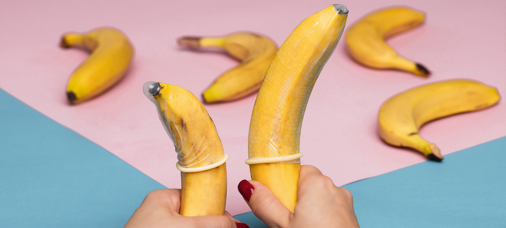 Zwei Bananen mit Kondomen vor buntem Hintergrund