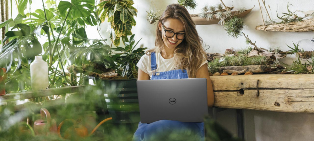 Frau mit Laptop sitzt zwischen Pflanzen und arbeitet