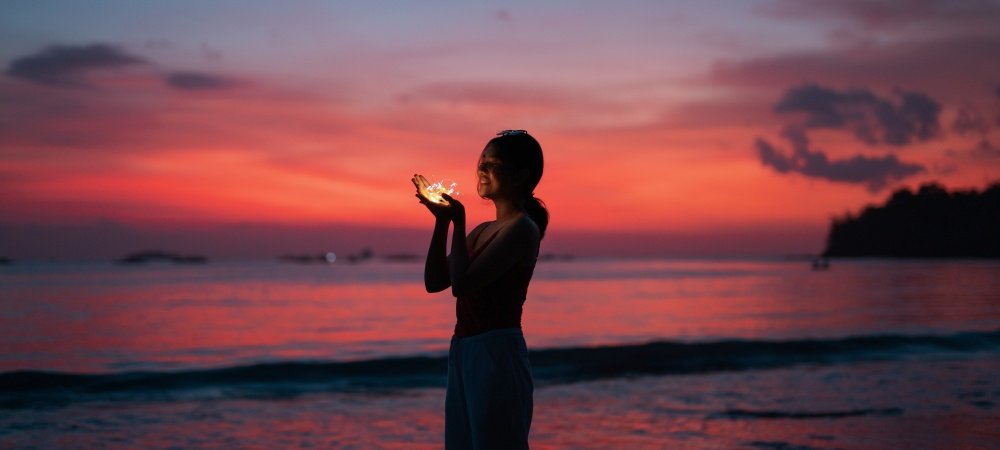 Frau am Strand mit Lichterkette in der Hand: Monatshoroskop Juni 2023