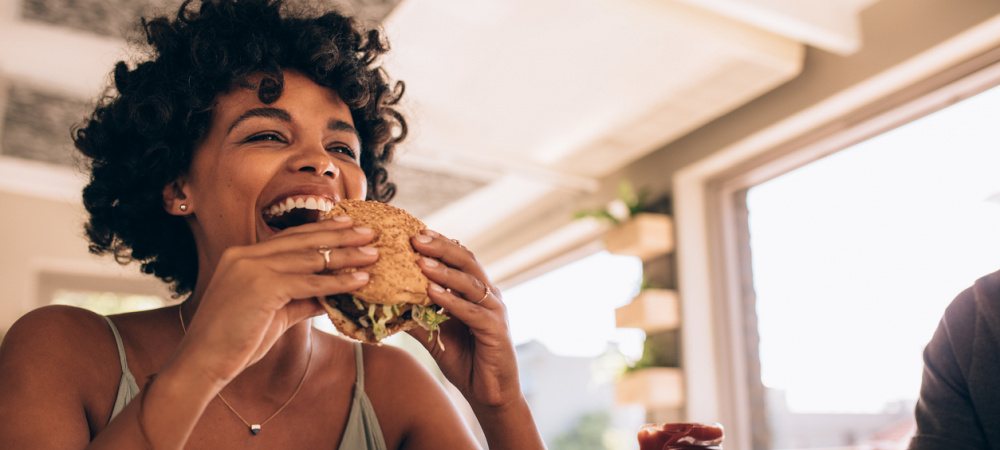 Frau isst Burger und lacht dabei