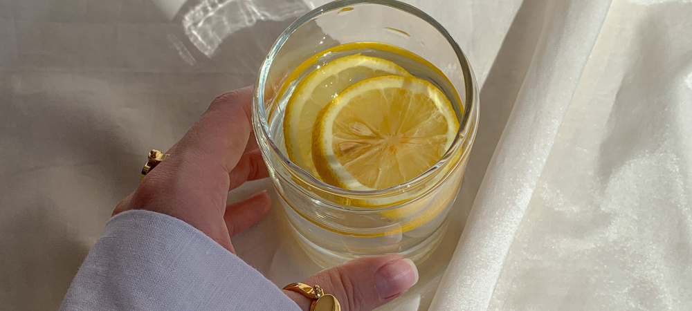 Hand mit Wasserglas und Zitronen