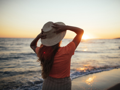 Eine Frau mit Hut schaut aufs Meer