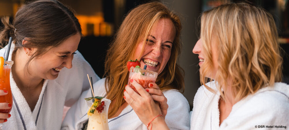 Drei junge Frauen lachen und trinken Cocktails