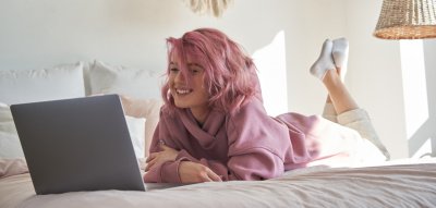 Teenie Mädchen mit rosa Haaren liegt im Bett und schaut auf den Laptop