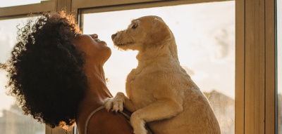 Frau steht am Fenster mit Hund auf dem Arm