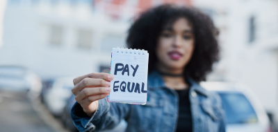 Frau hält Zettel hoch Equal Pay Day
