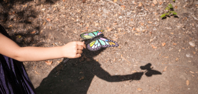Ein Kind spielt mit einem Papier-Schmetterling und seinem Schatten