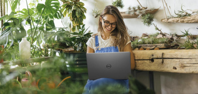Frau mit Laptop sitzt zwischen Pflanzen und arbeitet