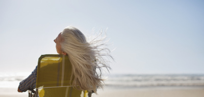 Frau mit grauen langen Haaren sitzt am Meer