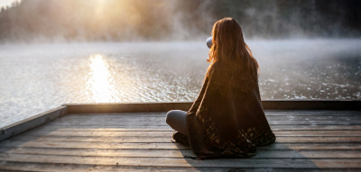 Frau sitzt zum Sonnenaufgang am See