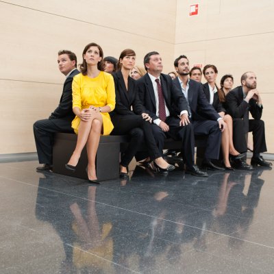 Wartende Business-Menschen unter ihnen eine Frau im knallgelben Kleid
