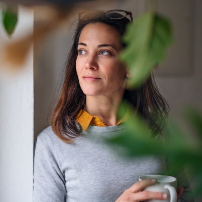 Frau mit Kaffee am Fenster, Grünpflanzen im Vordergrund