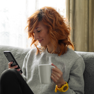 Frau mit Kaffee und Smartphone auf dem Sofa