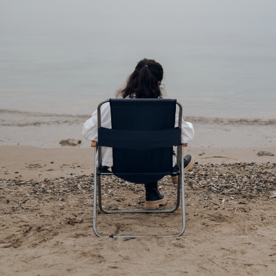 Frau sitzt auf Klappstuhl und schaut aufs Meer, Bare Minimum Monday