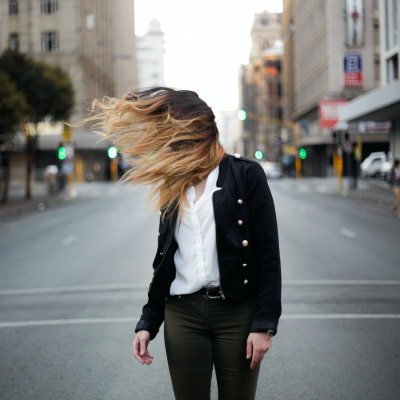 Frau steht auf der Straße, ihre Haare wehen zur Seite über ihr Gesicht