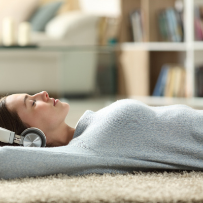 Junge Frau, die auf dem Teppichboden liegt und dabei Musik hört