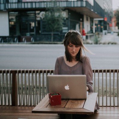 Frau sitzt mit Laptop im Cafe an einer Straße