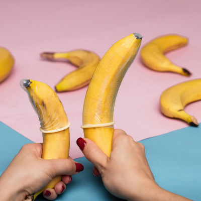 Zwei Bananen mit Kondomen vor buntem Hintergrund