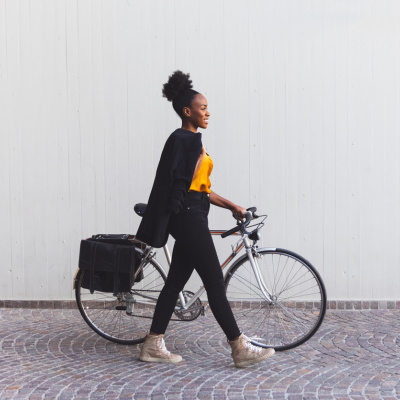 Eine Geschäftsfrau schiebt ihr Fahrrad durch die Stadt und trägt ihren Blazer über die Schulter
