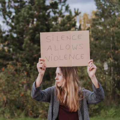 Frau hält Schild mit Aufschrift "Silence allows Violence" in die Kamera