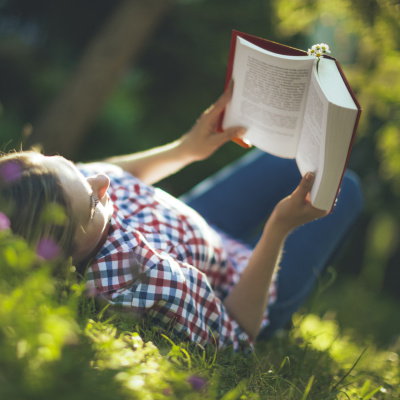 Junge Frau liest ein Buch und liegt dabei auf grüner Wiese
