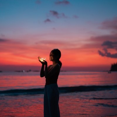 Frau am Strand mit Lichterkette in der Hand: Monatshoroskop Juni 2023