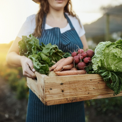 Frau steht auf dem Feld und hat frisch geerntetes Gemüse im Arm
